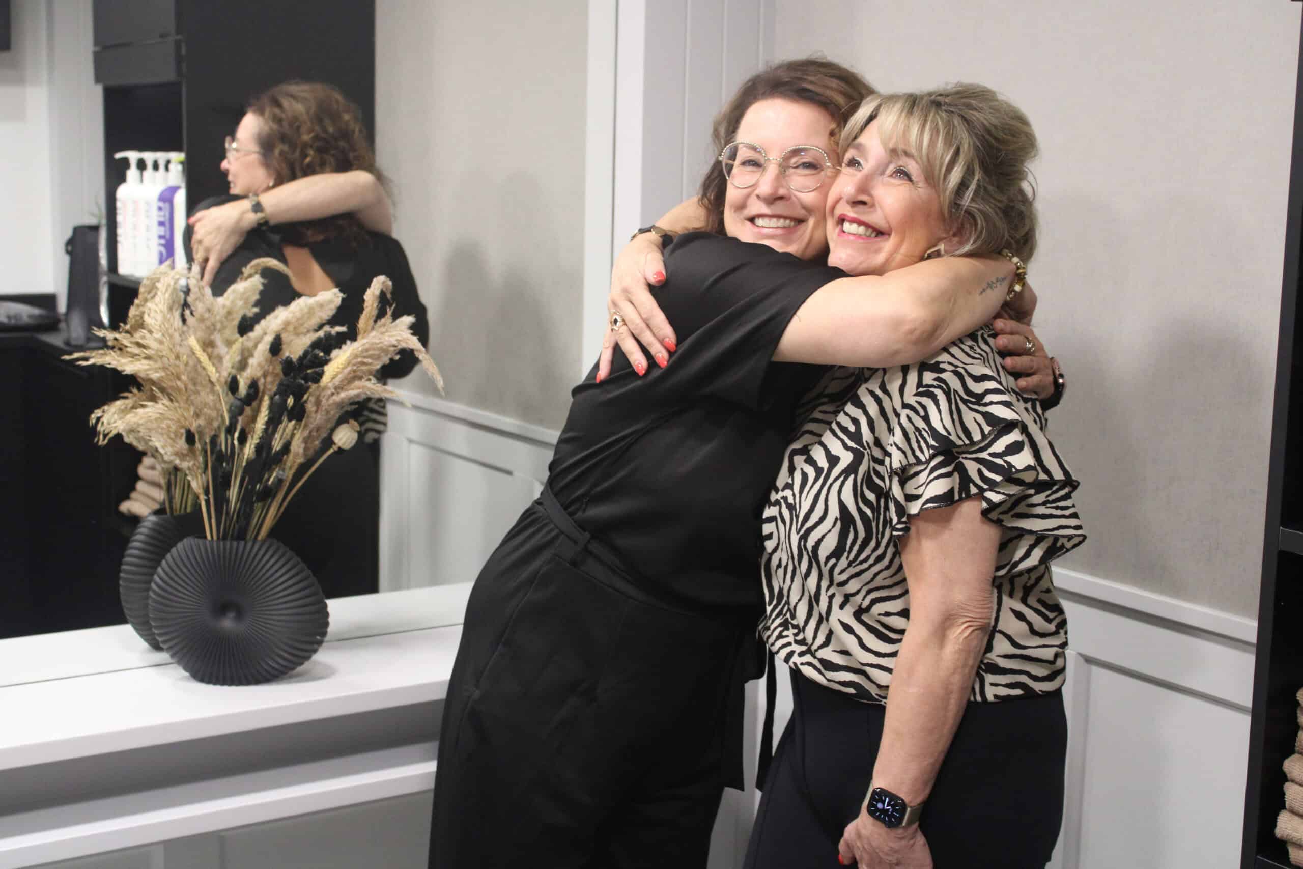 Eigenaar van Hairnation omarmt een tevreden klant in de salon.